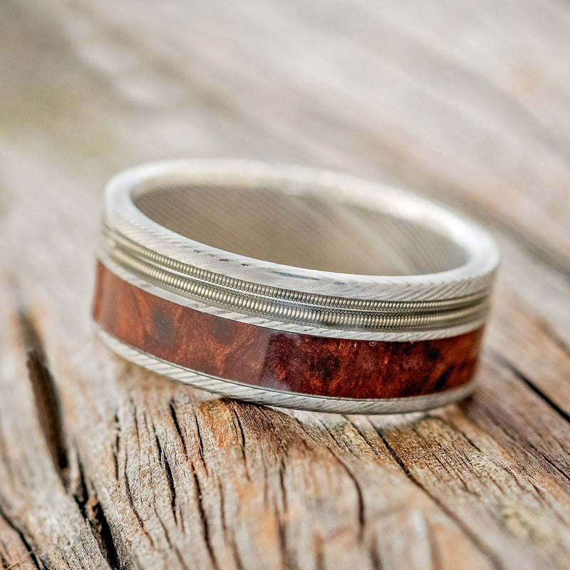 Shown here is "Raptor", a custom, handcrafted men's wedding ring featuring 2 channels with guitar string and redwood inlays, tilted left. Additional inlay options are available upon request.