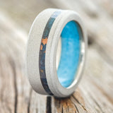 Shown here is "Vertigo", a custom, handcrafted men's wedding ring featuring a sandblasted titanium base, with an offset copper patina inlay and a turquoise lining, upright facing left. Additional inlay options are available upon request.