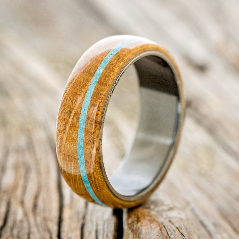 Shown here is "Remmy", a custom, handcrafted men's wedding ring featuring a whiskey barrel oak overlay and a turquoise inlay, shown here on a fire-treated black zirconium band, upright facing left. Additional inlay options are available upon request.