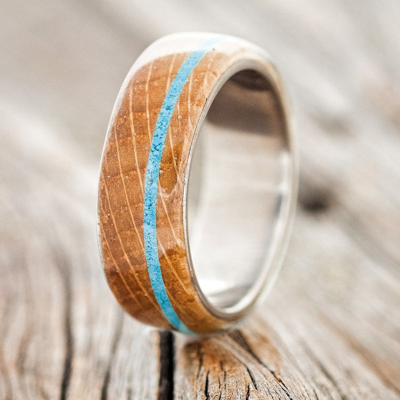 Shown here is "Remmy", a custom, handcrafted men's wedding ring featuring a whiskey barrel oak overlay & a turquoise inlay on a titanium band, upright facing left. Additional inlay options are available upon request.