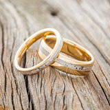 Shown here is a matching wedding band set featuring "Eterna" & "Vertigo", laying together. "Vertigo" is a handcrafted wedding band featuring an offset antler inlay. "Eterna" is a stacking-style wedding band featuring an antler inlay. Here, both rings are shown in 14K yellow gold bands. Additional inlay options are available upon request!