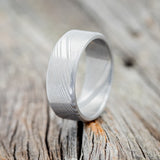 Shown here is a handcrafted men's wedding ring shown featuring a solid Damascus steel band, upright facing left.