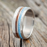 Shown here is "Cosmo", a custom, handcrafted men's wedding ring featuring ironwood and turquoise inlays, shown here on a hammered titanium band, upright facing left. Additional inlay options are available upon request.
