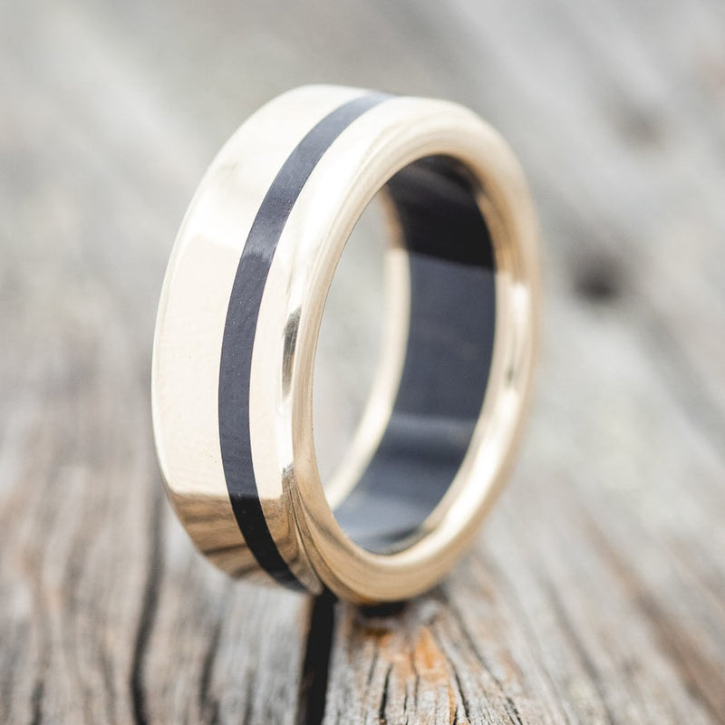 Shown here is "Vertigo", a handcrafted men's wedding ring featuring a jet stone lining and inlay on a 14K gold band, upright facing left. Additional inlay options are available upon request.