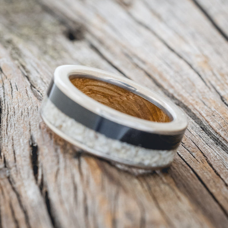 Shown here is "Flynn", a custom, handcrafted men's wedding ring featuring elk tooth & charred whiskey barrel oak inlays with a whiskey barrel lining, tilted left. Additional inlay options are available upon request.