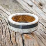 Shown here is "Flynn", a custom, handcrafted men's wedding ring featuring elk tooth & charred whiskey barrel oak inlays with a whiskey barrel lining, laying flat. Additional inlay options are available upon request.