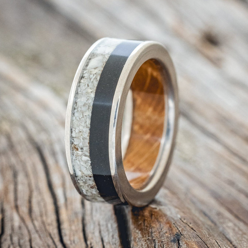 Shown here is "Flynn", a custom, handcrafted men's wedding ring featuring elk tooth & charred whiskey barrel oak inlays with a whiskey barrel lining, upright facing left. Additional inlay options are available upon request.