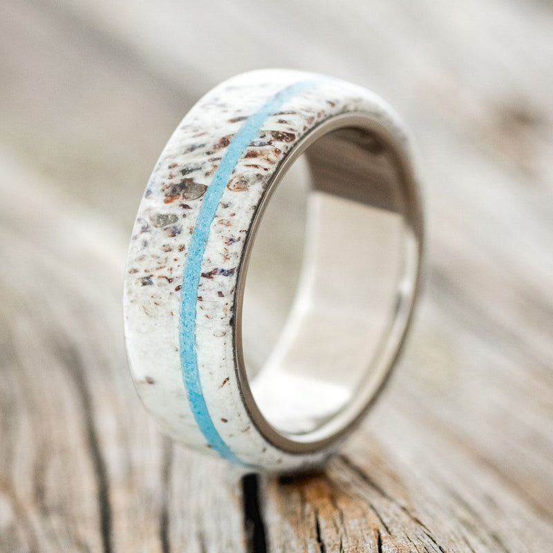 Shown here is "Remmy", a custom, handcrafted men's wedding ring featuring an antler overlay with a turquoise inlay, upright facing left. Additional inlay options are available upon request.
