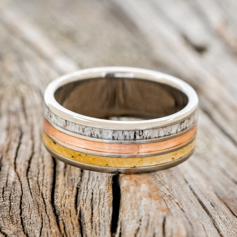 Shown here is "Rio", a custom, handcrafted men's wedding ring featuring 3 channels with spalted maple wood, rustic copper, and elk antler inlays on a titanium band, laying flat. Additional inlay options are available upon request.