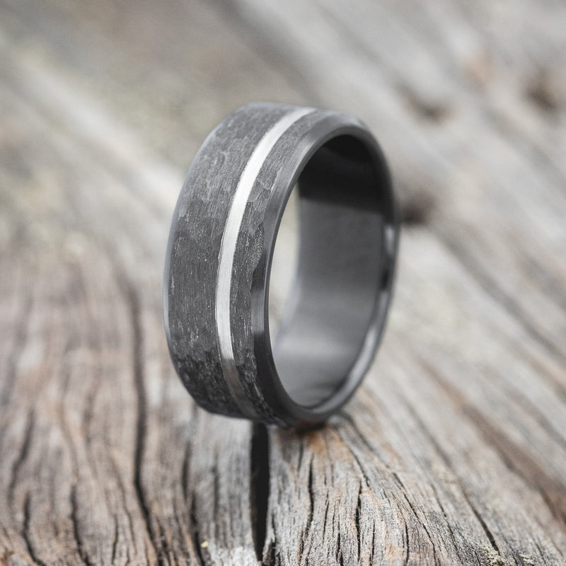 Shown here is a handcrafted men's wedding ring shown featuring a hammered black zirconium band with an offset cut etching, upright facing left