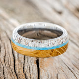 Shown here is "Banner", a custom, handcrafted men's wedding ring featuring whiskey barrel oak and antler overlay with a turquoise inlay, laying flat. Additional inlay options are available upon request.