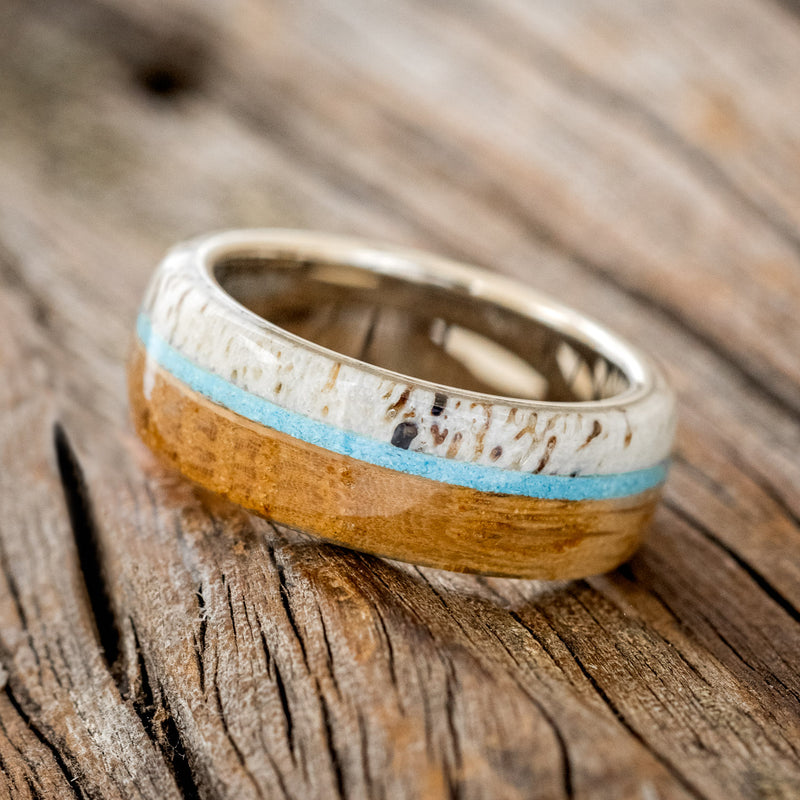 Shown here is "Banner", a custom, handcrafted men's wedding ring featuring whiskey barrel oak and antler overlay with a turquoise inlay, tilted left. Additional inlay options are available upon request.