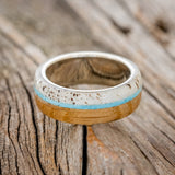 Shown here is "Banner", a custom, handcrafted men's wedding ring featuring whiskey barrel oak and antler overlay with a turquoise inlay, laying flat. Additional inlay options are available upon request.
