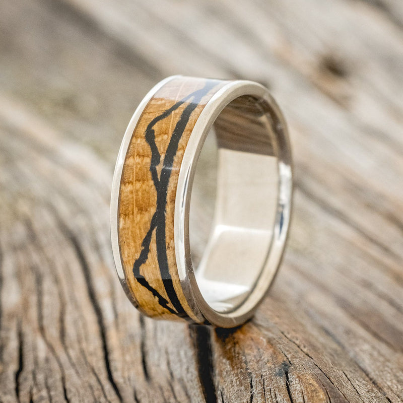 Shown here is "The Expedition", a custom, handcrafted men's wedding ring featuring a mountain engraving with whiskey barrel oak and charred whiskey barrel inlays, upright facing left. Additional inlay options are available upon request.