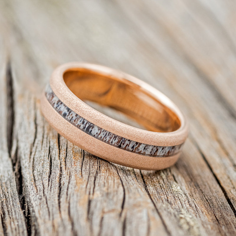 Shown here is "Vertigo", a custom, handcrafted men's wedding ring featuring an offset antler inlay on a sandblasted 14K gold band, tilted left. Additional inlay options are available upon request.