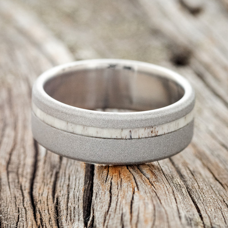 Shown here is "Vertigo", a custom, handcrafted men's wedding ring featuring an antler inlay with a sandblasted finish, laying flat. Additional inlay options are available upon request.