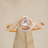 Shown here is "Charlotte", a round cut morganite twisted women's engagement ring with a diamond halo and diamond accents.