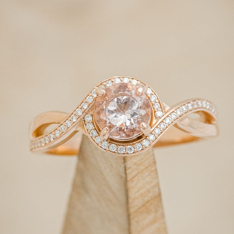 Shown here is "Charlotte", a round cut morganite twisted women's engagement ring with a diamond halo and diamond accents.