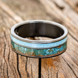 Shown here is "Raptor", a custom, handcrafted men's wedding ring featuring a patina copper and turquoise inlay on a fire-treated black zirconium band, laying flat. Additional inlay options are available upon request.