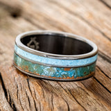 Shown here is "Raptor", a custom, handcrafted men's wedding ring featuring a patina copper and turquoise inlay on a fire-treated black zirconium band, tilted left. Additional inlay options are available upon request.