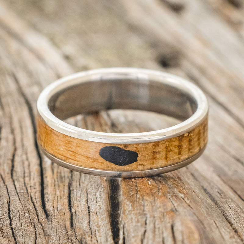 Shown here is "Rainier", a custom, handcrafted men's wedding ring featuring a whiskey barrel oak and charred whiskey barrel inlay on a titanium band, laying flat. Additional inlay options are available upon request.