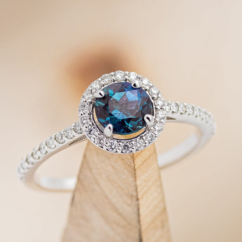 Shown here is The "Aurora", a round cut lab-created alexandrite women's engagement ring with a diamond halo and diamond accents.
