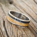 Shown here is "Raptor", a custom, handcrafted men's wedding ring featuring authentic whiskey barrel oak and charred whiskey barrel inlays, tilted left. Additional inlay options are available upon request.
