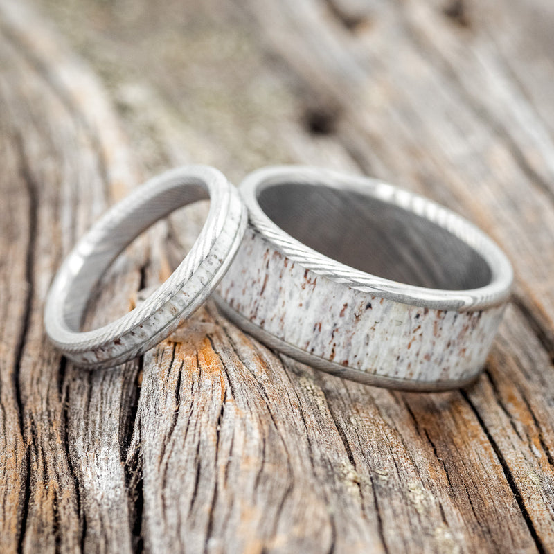 Shown here is a matching wedding band set featuring "Eterna" & "Rainier", laying together. "Rainier" is a handcrafted wide wedding band featuring antler inlay. "Eterna" is a stacking-style wedding band featuring antler inlay. Here, they are shown on Damascus steel bands.