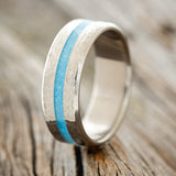 Shown here is "Nirvana", a custom, handcrafted men's wedding ring featuring a centered turquoise inlay and a hammered finish, upright facing left. Additional inlay options are available upon request.