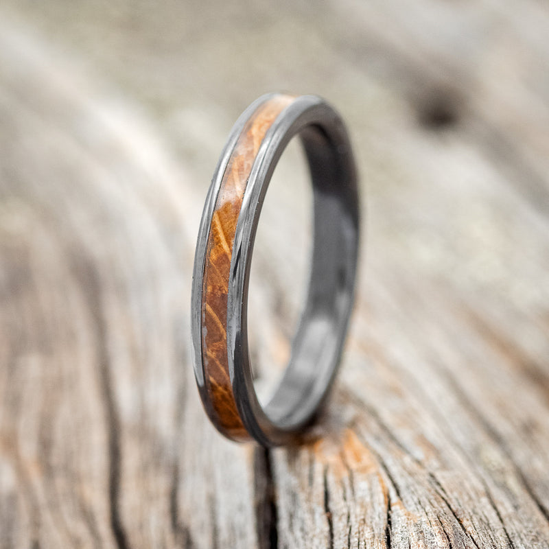 Shown here is "Eterna", a custom, handcrafted women's stacking band featuring a whiskey barrel inlay, shown here on a fire-treated black zirconium band, upright facing left. Additional inlay options are available upon request.