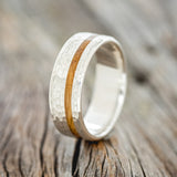 Shown here is "Vertigo", a custom, handcrafted men's wedding ring featuring a whiskey barrel inlay with a hammered finish, upright facing left. Additional inlay options are available upon request.