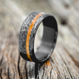 Shown here is "Vertigo", a custom, handcrafted men's wedding ring featuring a whiskey barrel inlay on a hammered, fire-treated black zirconium band, upright facing left. Additional inlay options are available upon request.