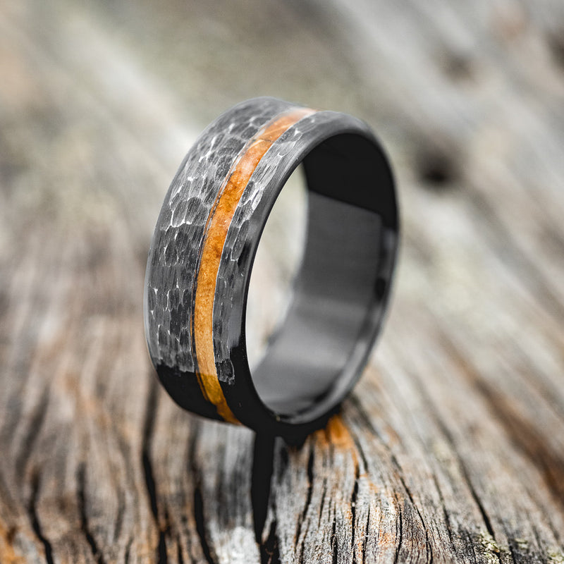 Shown here is "Vertigo", a handcrafted men's wedding ring featuring a whiskey barrel wood inlay with a hammered finish, upright facing left.
