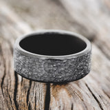 Shown here is a handcrafted men's wedding ring featuring a fire-treated black zirconium band with a hammered finish, laying flat.