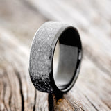 Shown here is a handcrafted men's wedding ring featuring a fire-treated black zirconium band with a hammered finish, upright facing left.