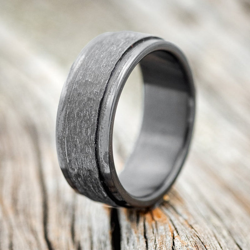 Shown here is "Sedona", a handcrafted men's wedding ring featuring a solid, fire-treated, black zirconium band with a raised, hammered center, upright facing left. 
