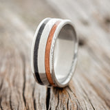 Shown here is "Ryder", a custom, handcrafted men's wedding ring featuring powdered copper and jet stone inlays on a Damascus steel band, upright facing left. Additional inlay options are available upon request.