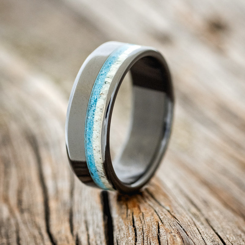 Shown here is "Castor", a custom, handcrafted men's wedding ring featuring a hand-crushed turquoise and antler inlay, shown here on a fire-treated black zirconium band, upright facing left. Additional inlay options are available upon request.
