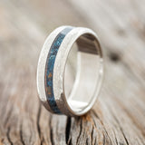 Shown here is "Nirvana", a custom, handcrafted men's wedding ring featuring a centered patina copper inlay and a hammered finish, upright facing left.