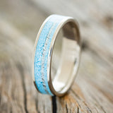 Shown here is "Rainier", a custom, handcrafted men's wedding ring featuring turquoise and offset antler inlay on a titanium band, upright facing left. Additional inlay options are available upon request.