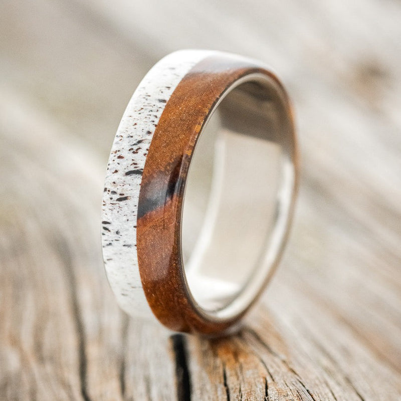 Shown here is "Arlo", a handcrafted men's wedding ring featuring an ironwood and an antler overlay on a titanium band, upright facing left. Additional overlay options are available upon request.
