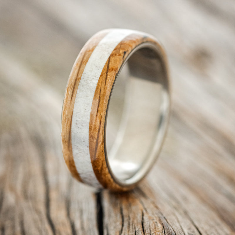 Shown here is "Canyon", a custom, handcrafted men's wedding ring featuring an antler inlay set between two whiskey barrel oak overlays, upright facing left. Additional inlay and overlay options are available upon request.