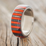 Shown here is "Haven", a custom, handcrafted men's wedding ring featuring birch wood overlay that has been dyed red and black, upright facing left. Additional overlay options are available upon request.