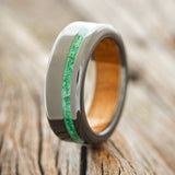 Shown here is "Vertigo", a handcrafted men's wedding ring featuring a whiskey barrel lined, black zirconium band with a malachite inlay, upright facing left. Additional inlay and lining options are available upon request.