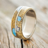 Shown here is "Golden", a custom, handcrafted men's wedding ring featuring a buckeye burl overlay with turquoise and fire & ice opal inlays filling the burls, upright facing left. Additional inlay options are available upon request.