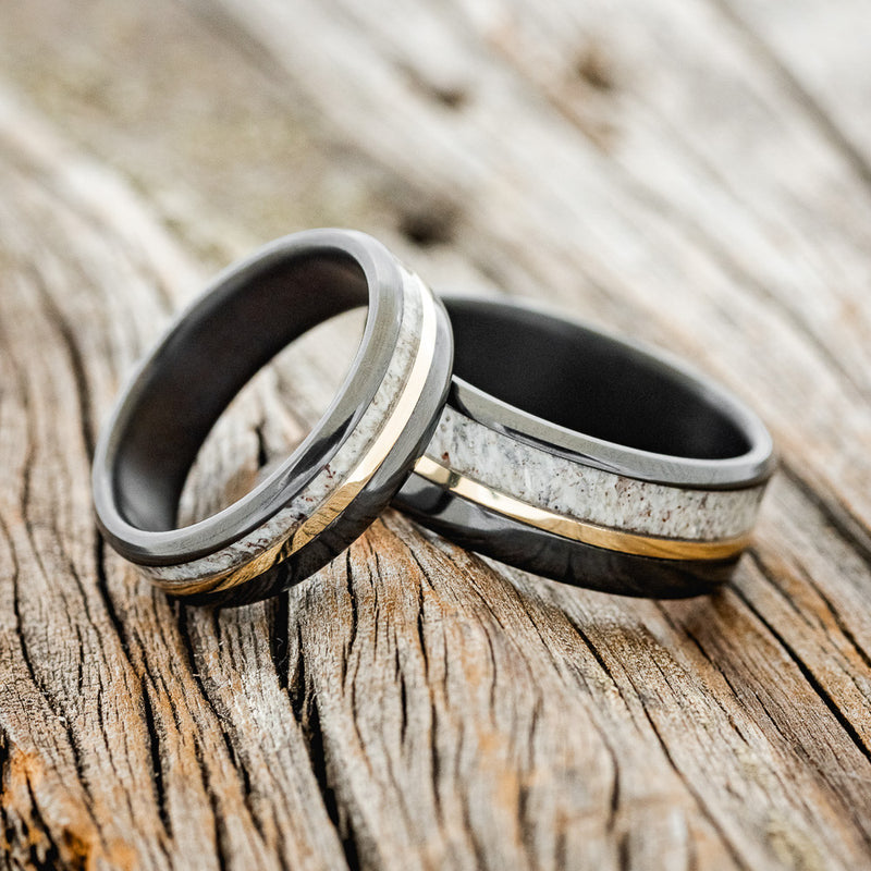 Shown here is a matching wedding band set featuring two "Tanner" rings with antler and 14K yellow gold inlays, shown here on fire-treated black zirconium bands, laying together.