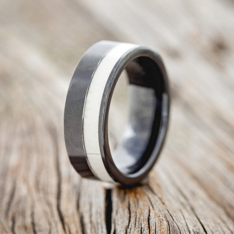 Shown here is "Castor", a custom, handcrafted men's wedding ring featuring an antler inlay on a black ceramic band, upright facing left. Additional inlay options are available upon request.