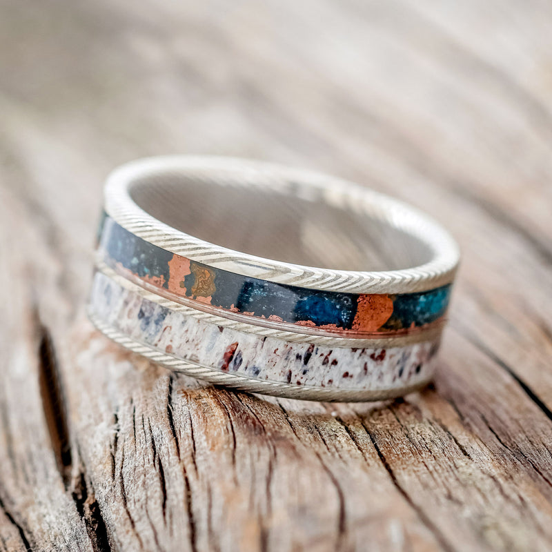 Shown here is "Dyad", a custom, handcrafted men's wedding ring featuring 2 channels with patina copper & antler inlays, tilted left. Additional inlay options are available upon request.