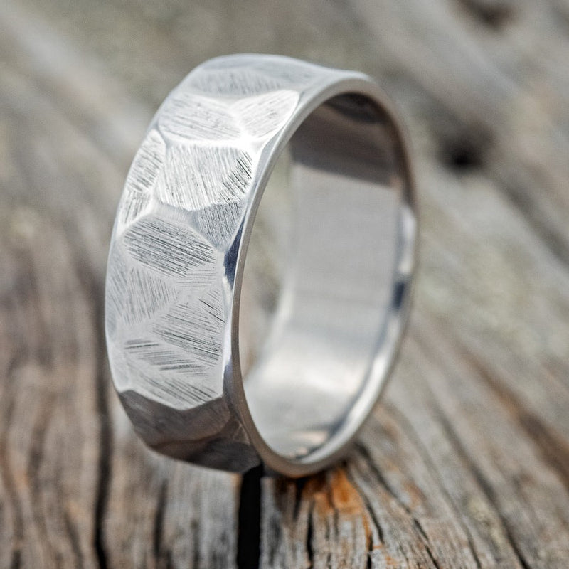 Shown here is a handcrafted men's wedding ring featuring a faceted band and a textured finish, upright facing left. Additional inlay options are available upon request.