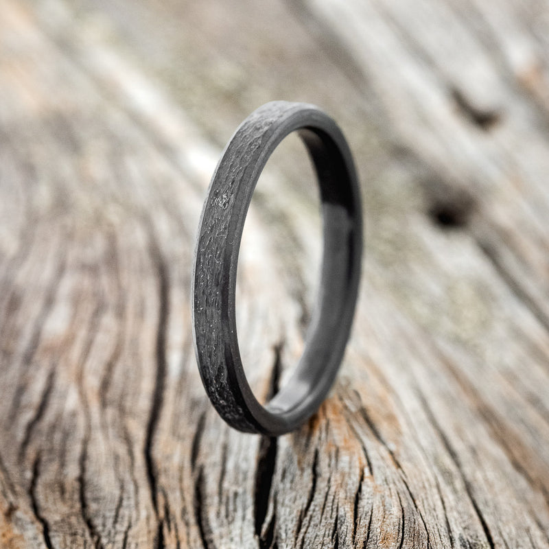 Shown here is a custom, handcrafted women's black zirconium stacking band featuring a hammered finish, upright facing left. 